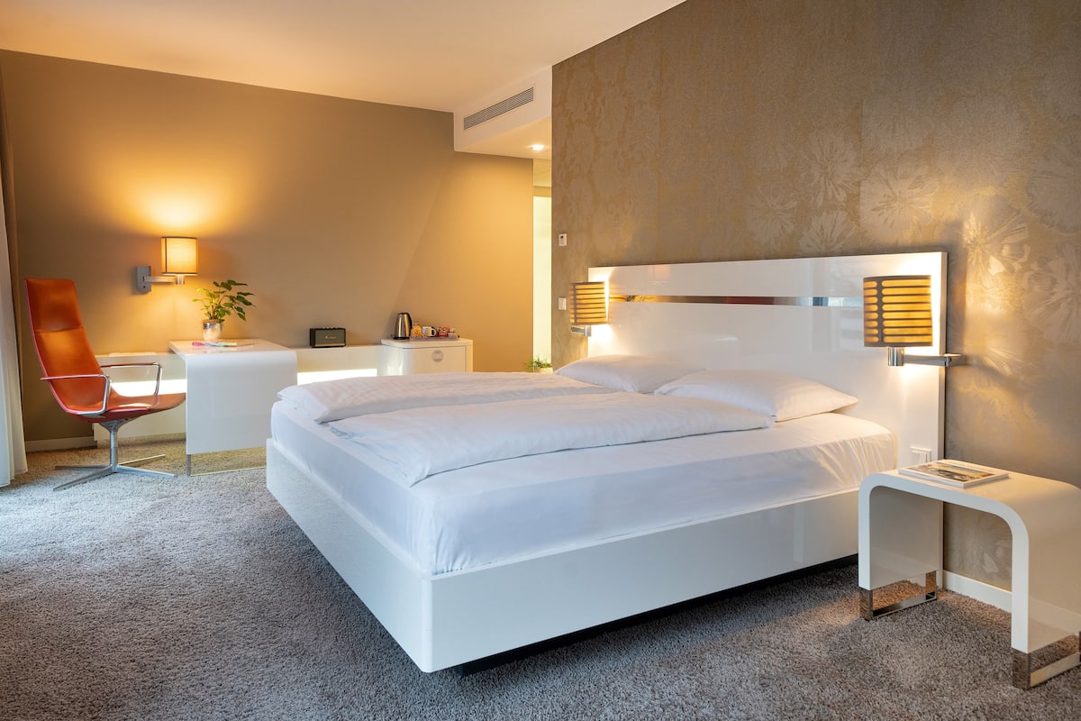 Una habitación de hotel moderna con una cama grande, un escritorio, una silla y dos lámparas fijadas a la pared.