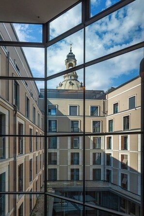 Une vue à travers la fenêtre d’un bâtiment doté d’une cour intérieure, avec une structure en forme de dôme visible au fond.
