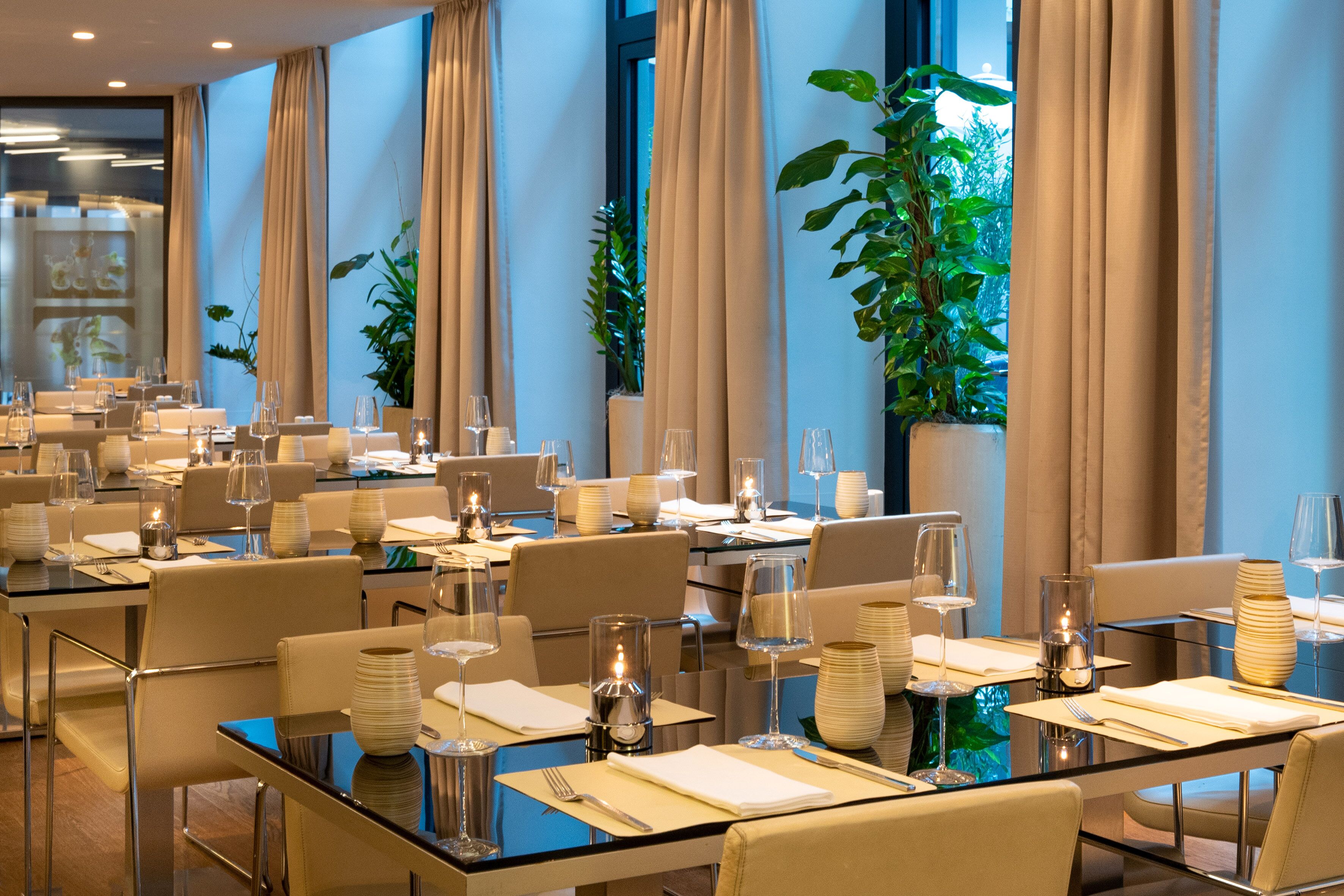 Un comedor bien iluminado con mesas dispuestas para varios comensales, que incluye cristalería, servilletas y velas.