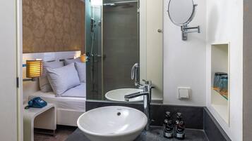 Ein modernes Badezimmer mit einem großen weißen Waschbecken, einer Duschkabine aus Glas, einem Spiegel und einem Nachttisch mit einer Lampe.