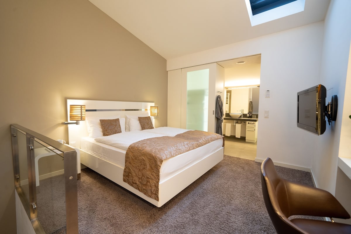 Una habitación de hotel moderna con una cama grande, un escritorio y un baño visible a través de una puerta abierta.
