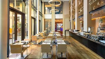 A modern hotel lobby with a long reception desk, multiple seating areas, and a buffet.