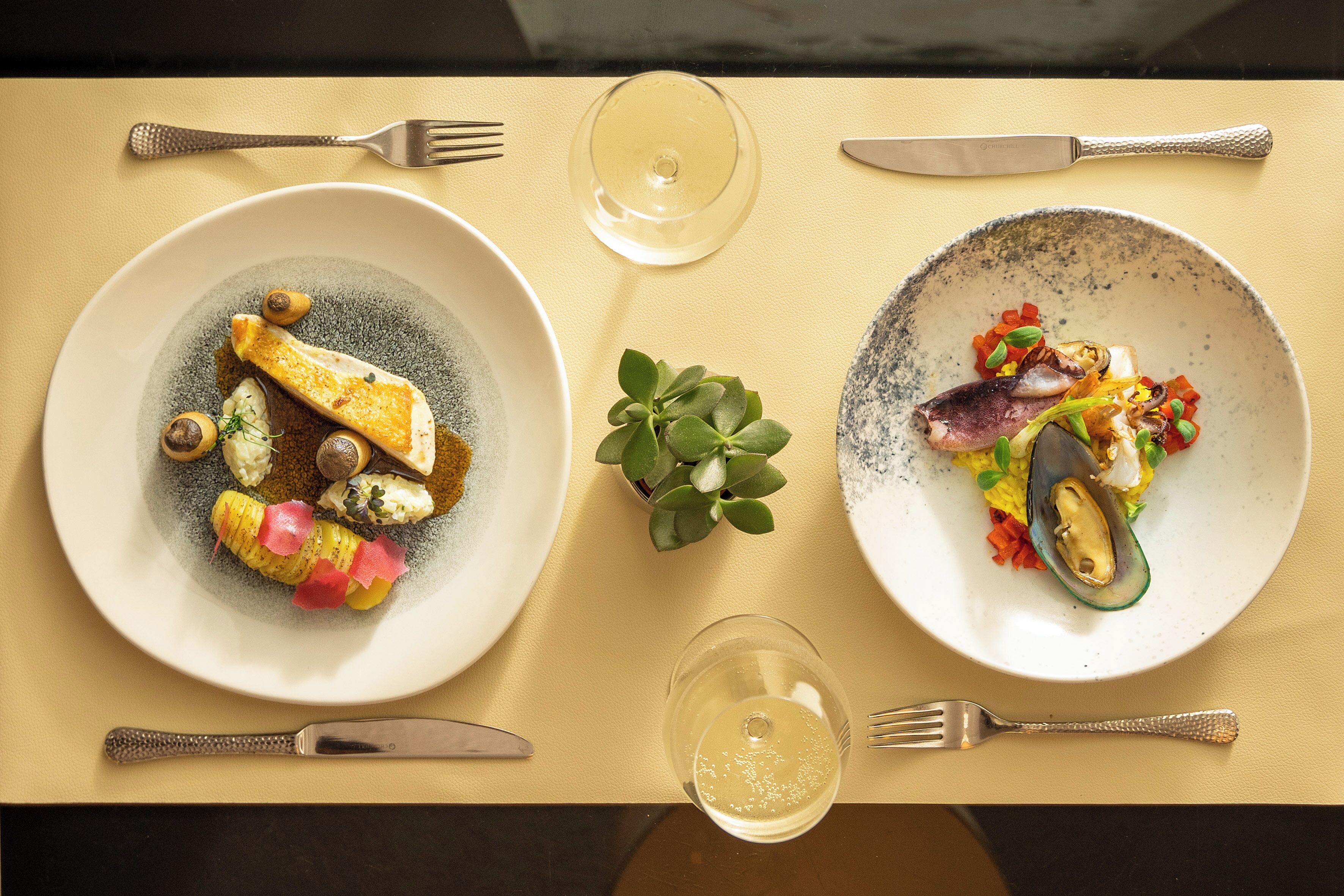 Two plates of food on a table with cutlery and glasses.