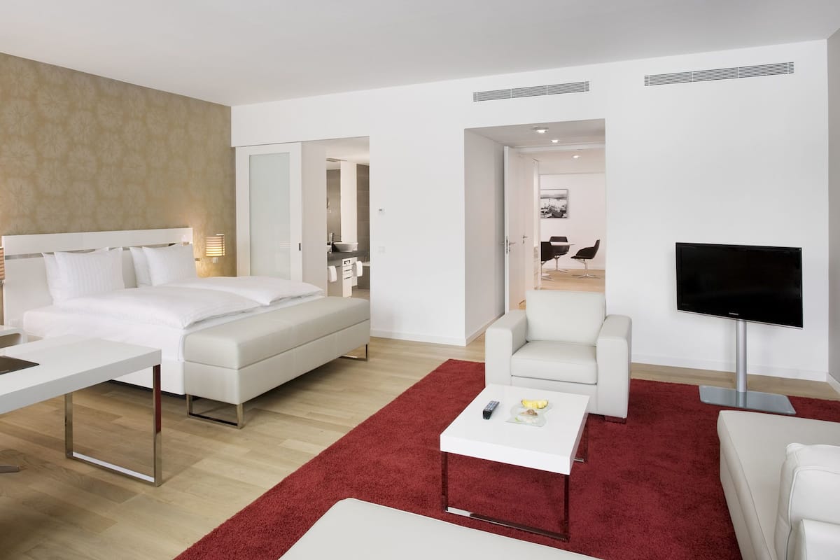 Una habitación de hotel moderna con cama, escritorio, televisor y alfombra roja.