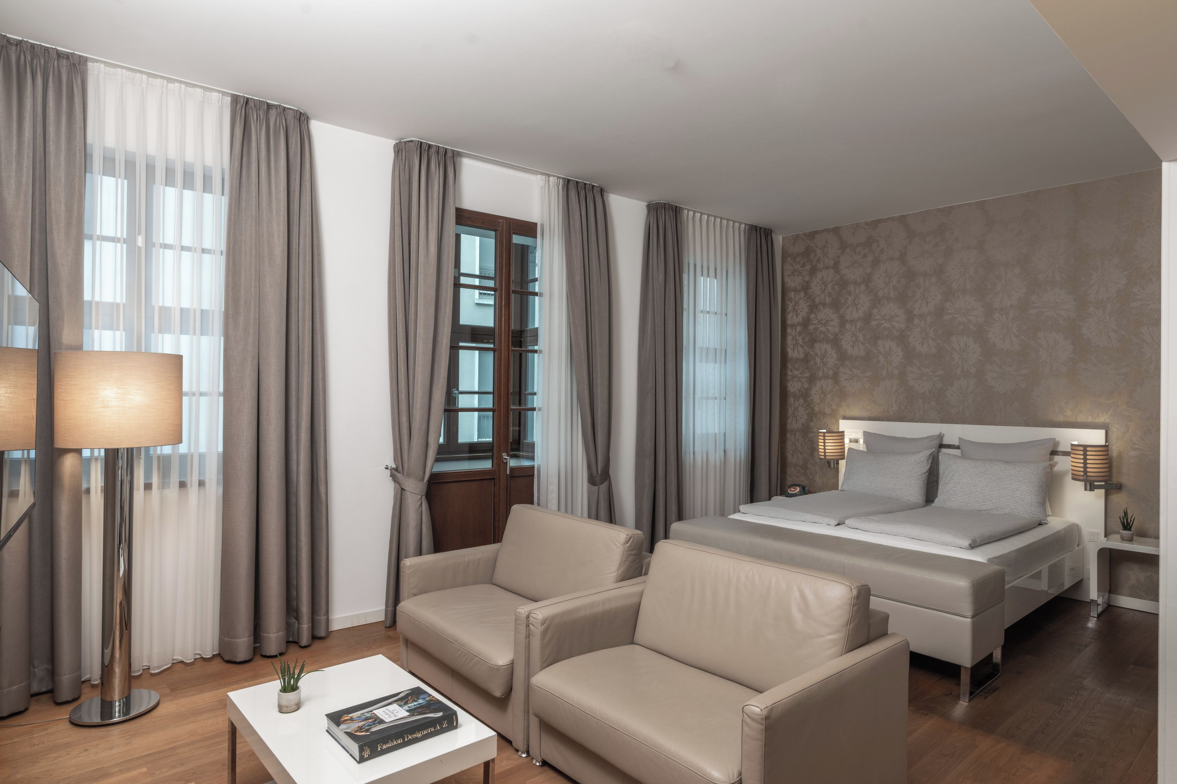 A hotel room with a bed, two armchairs, a coffee table, and a lamp.