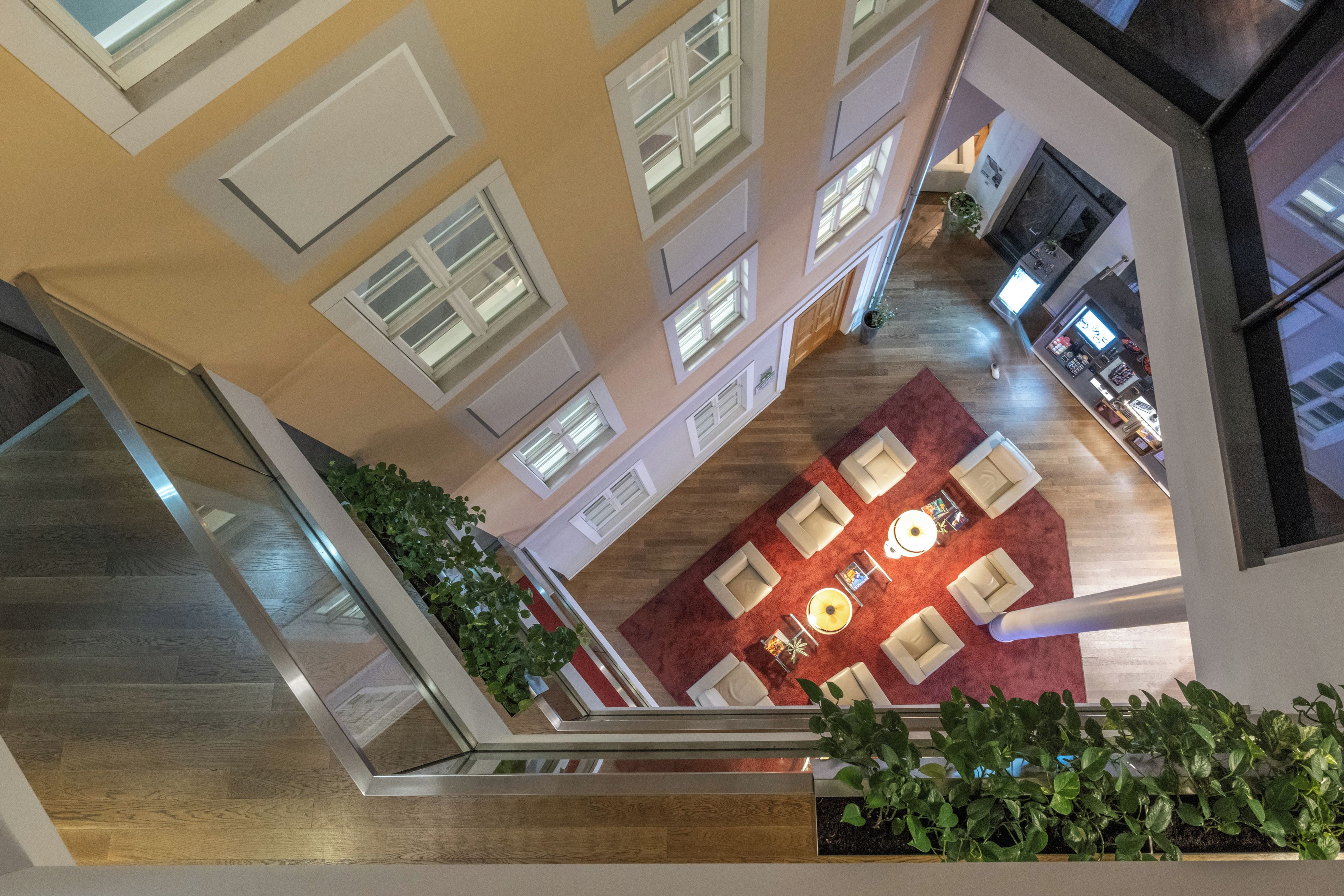 Un interior con techos altos, una zona de estar central, varias ventanas y una escalera.