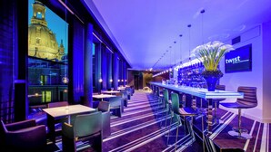 Eine moderne Bar mit einer langen Theke, Barhocker und einer großen Blumenvase.