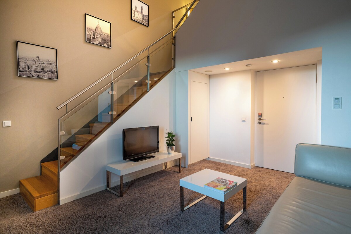 Een moderne woonkamer met een trap, een flatscreen televisie, een salontafel en een bank.
