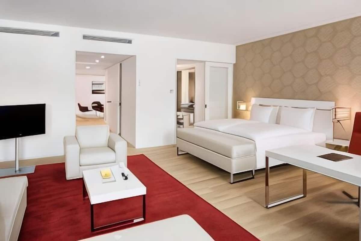 A hotel room with a bed, a desk, a chair, a TV, and a red carpet.