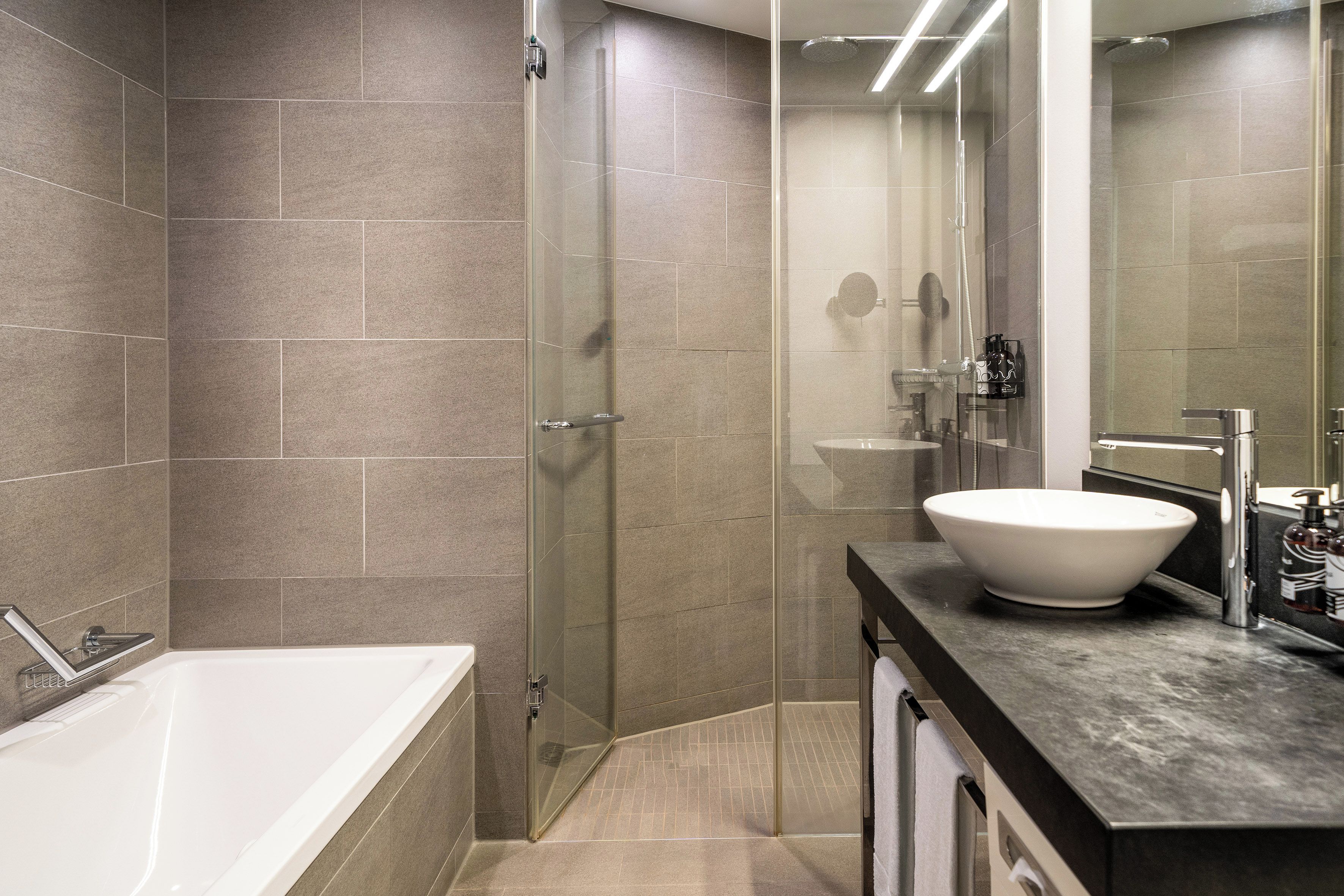 A modern bathroom with a glass-enclosed shower, a white bathtub, and a large mirror above the sink.