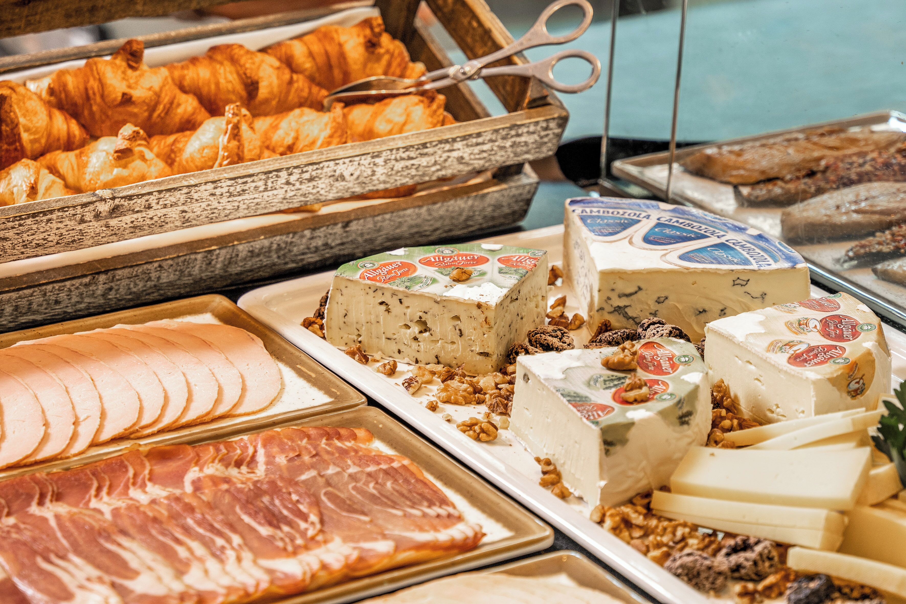 A variety of cheeses, meats, and pastries displayed in a deli setting.