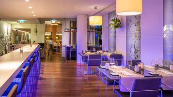 Ein modernes Restaurant mit langer Bar, mehreren Speisetischen und hängenden Pflanzen.