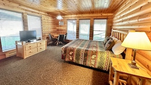 A log cabin room with a bed, desk, chair, television, and a lamp.