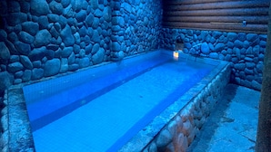 A stone-walled indoor swimming pool with a tiled floor and a wooden ceiling.