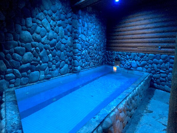 A stone-walled indoor swimming pool with a tiled floor and a wooden ceiling.