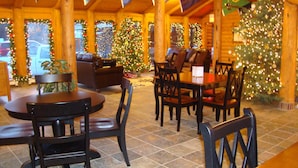 A cozy indoor area with wooden furniture, including a round table and chairs, and a Christmas tree decorated with lights and ornaments.