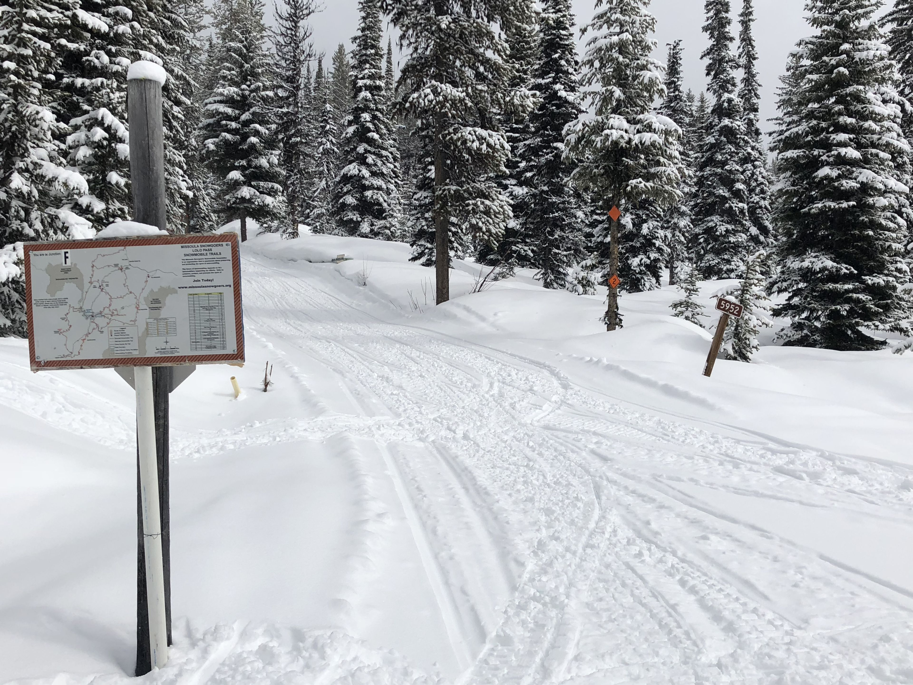Sendero cubierto de nieve con un poste señalizador que indica un mapa e información sobre la ruta.