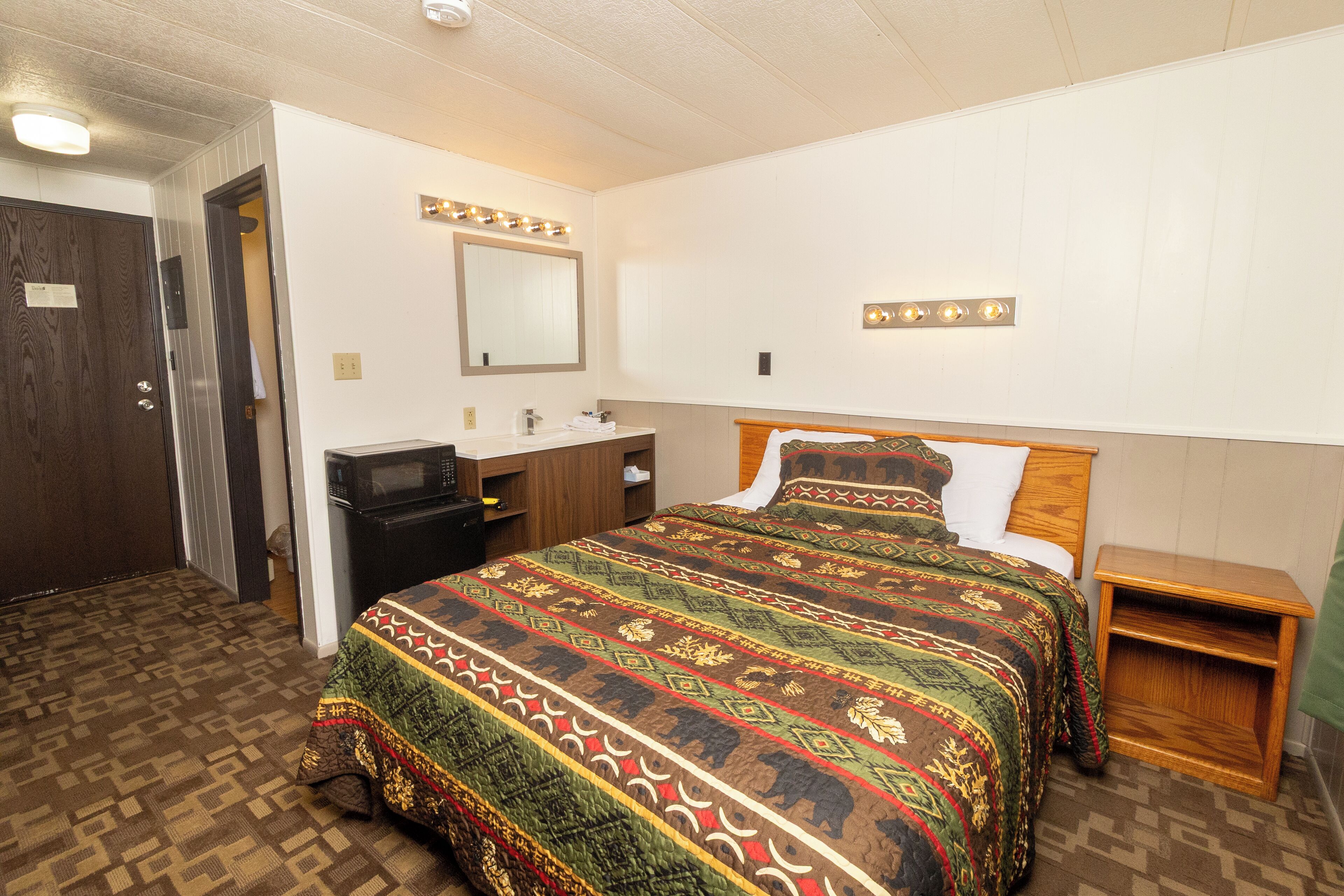 Un dormitorio con una cama grande, una mesita de noche de madera, un aparador y un espejo con luces.