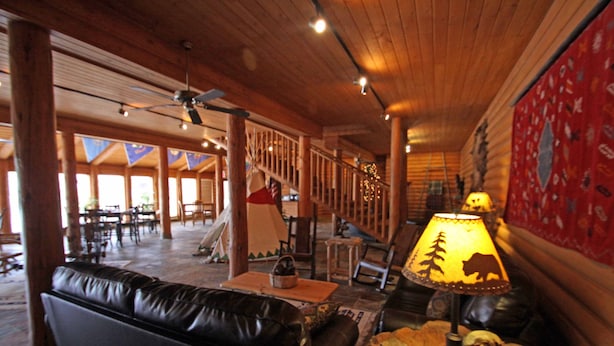 A cozy lobby with a leather sofa, a wooden coffee table, and a lamp with a bear silhouette. A staircase with a railing leads to another area.