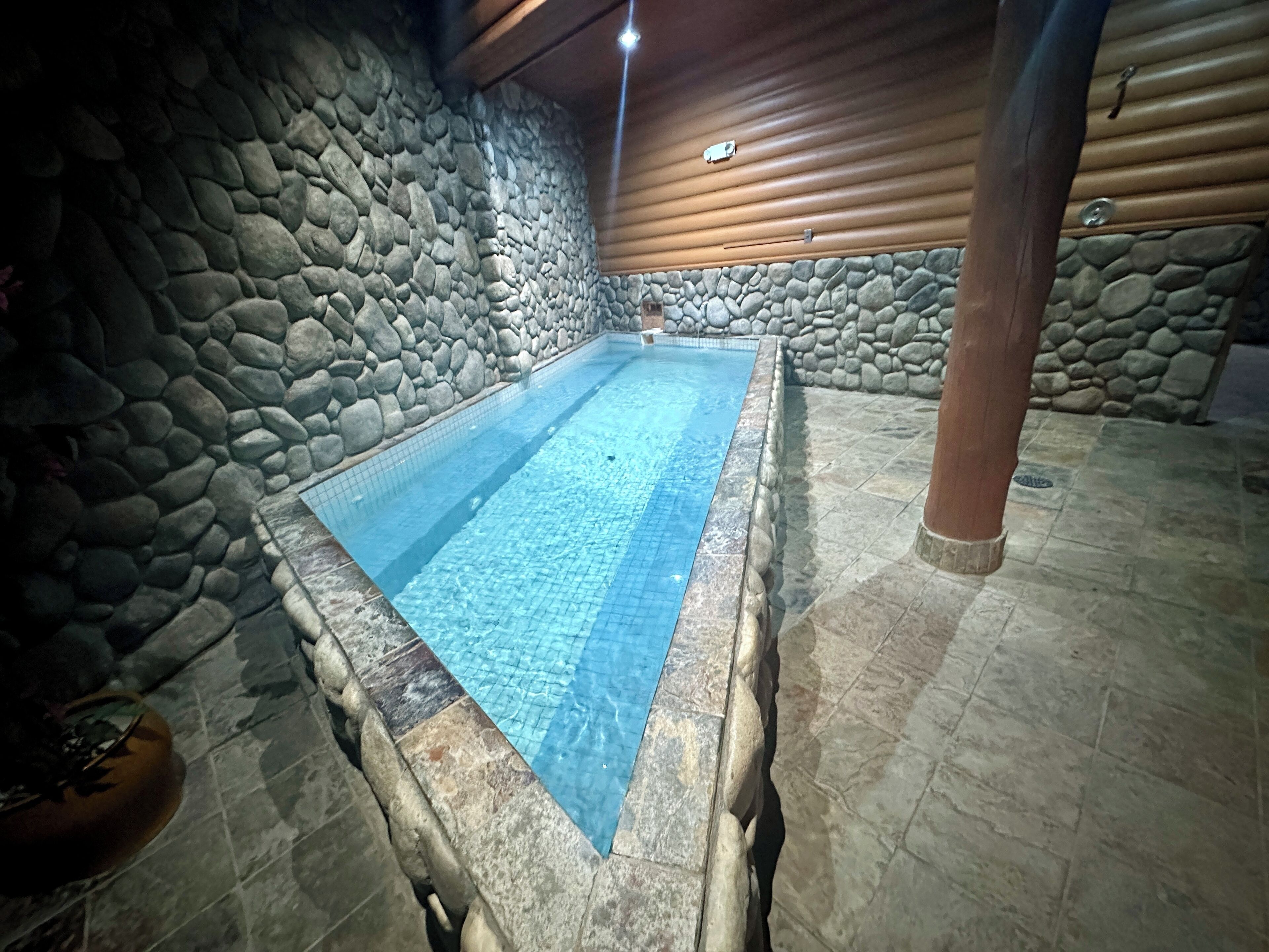 Une piscine intérieure aux murs de pierre, avec une eau d’un bleu limpide, entourée d’un sol et de murs en pierre.