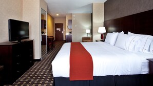 A hotel room with a large bed, a television on a dresser, a desk with a lamp, and a view of the hallway. - Holiday Inn Express Hotel & Suites AMITE by IHG (Amite)