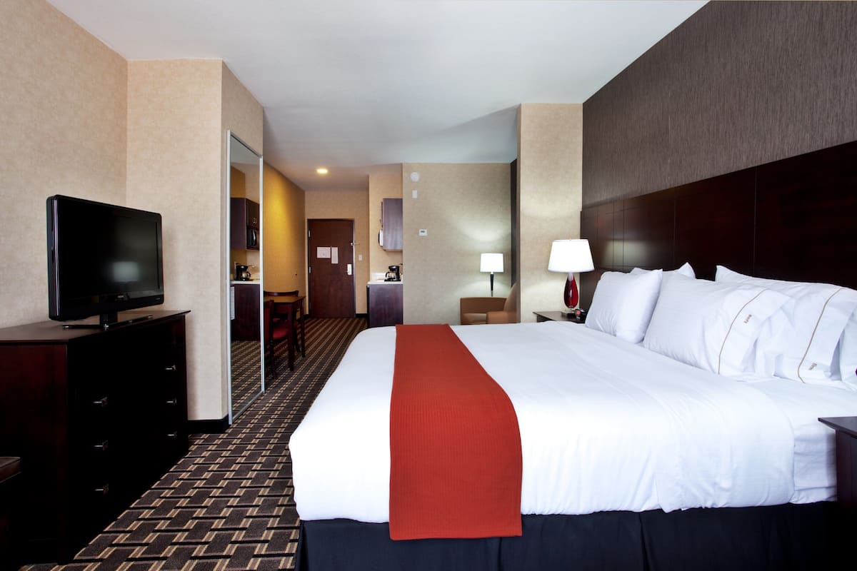 A hotel room with a large bed, a television on a dresser, a desk with a lamp, and a view of the hallway.