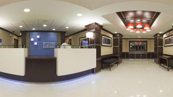 A hotel reception area with a curved reception desk, a digital display, and a seating area with a bench. - Holiday Inn Express Hotel & Suites AMITE by IHG (Amite)