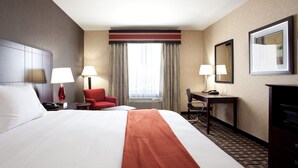 A hotel room with a large bed, two bedside lamps, a desk with a chair, a red chair, a large mirror, and a window with curtains. - Holiday Inn Express Hotel & Suites AMITE by IHG (Amite)
