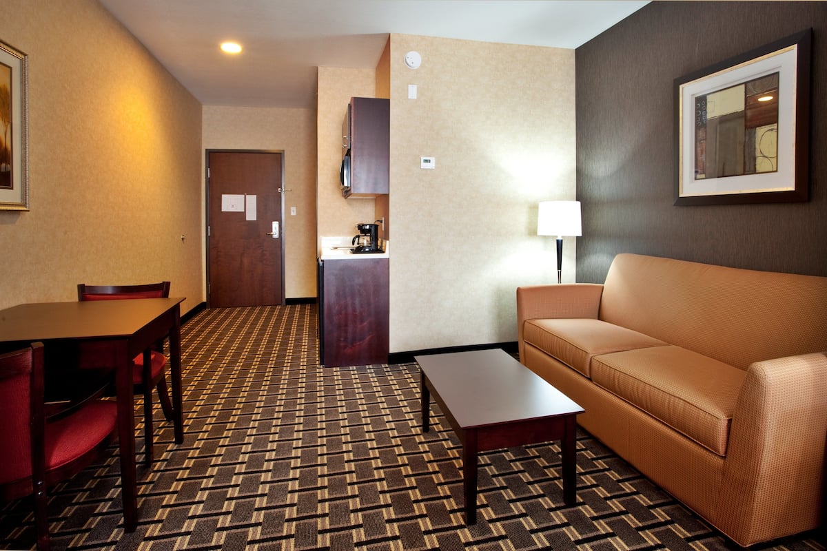 A hotel room with a dining table, a sofa, a coffee machine, and a lamp.