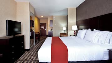 A hotel room with a large bed, a television on a dresser, a desk with a lamp, and a view into the kitchen area.