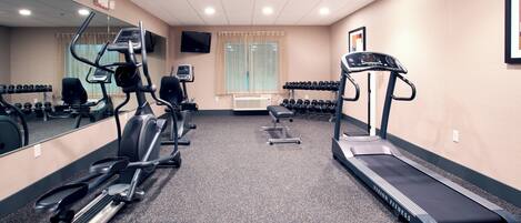 A gym with treadmills, elliptical machines, and a mirrored wall.