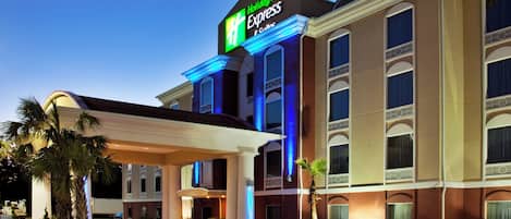 A Holiday Inn Express hotel with a covered entrance, palm trees, and a clear sky.