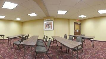 A conference room with six tables and chairs, a framed picture on the wall, and a door with a sign.