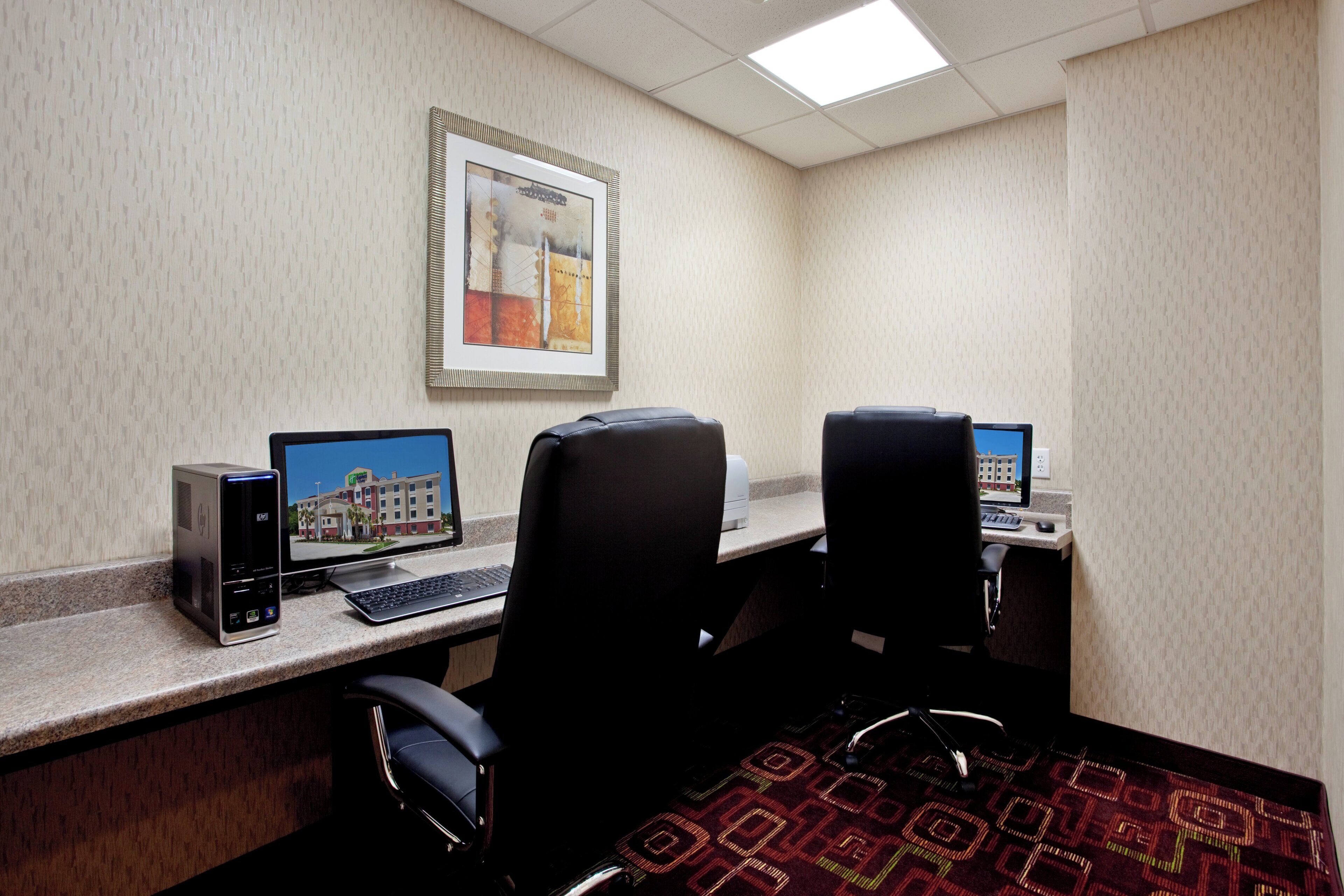 A hotel room with two desks, each with a computer and keyboard, and a framed picture on the wall.