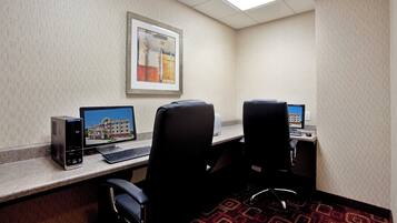 A hotel room with two desks, each with a computer and keyboard, and a framed picture on the wall.
