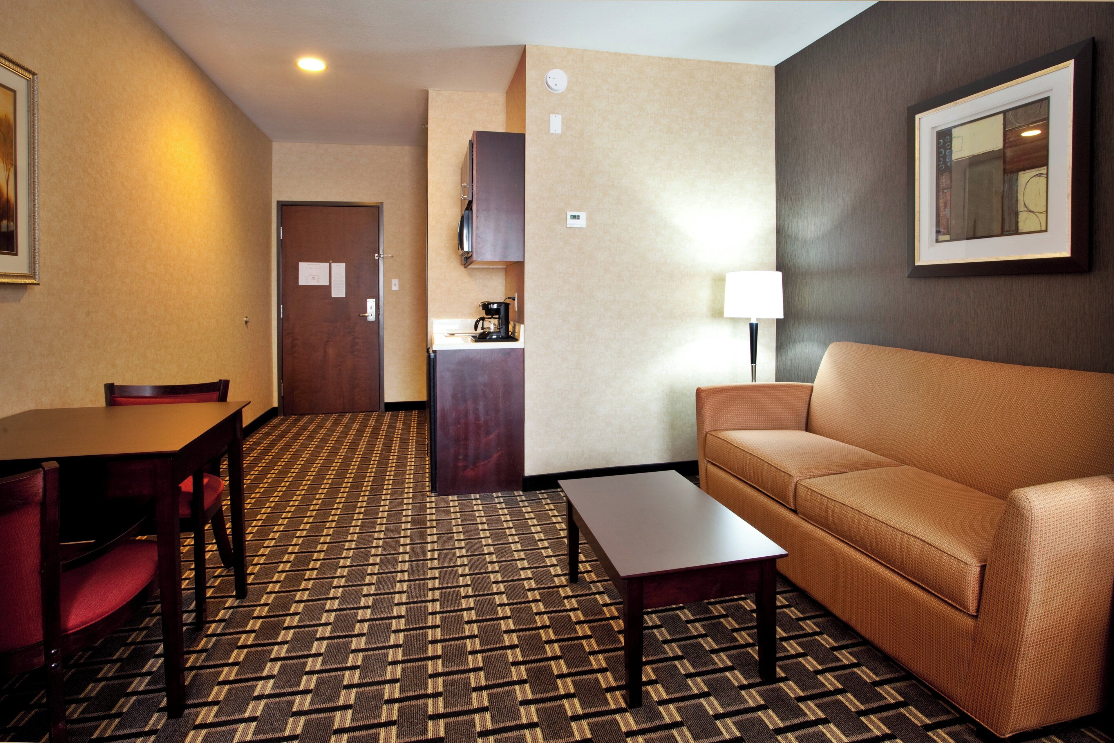 A hotel room with a dining table, a sofa, a coffee table, a kitchenette, and a framed picture on the wall.
