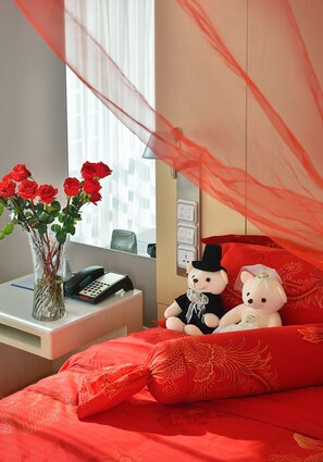 A hotel room with a bed, a bedside table with a vase of flowers, a telephone, and a decorative canopy. - Hanting Hotel (Beijing)
