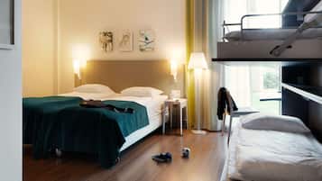 A hotel room with a bed, a bunk bed, a bedside table, a lamp, and artwork on the wall.