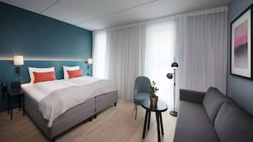A modern hotel room with a bed, a sofa, a chair, a small table, and a floor lamp.
