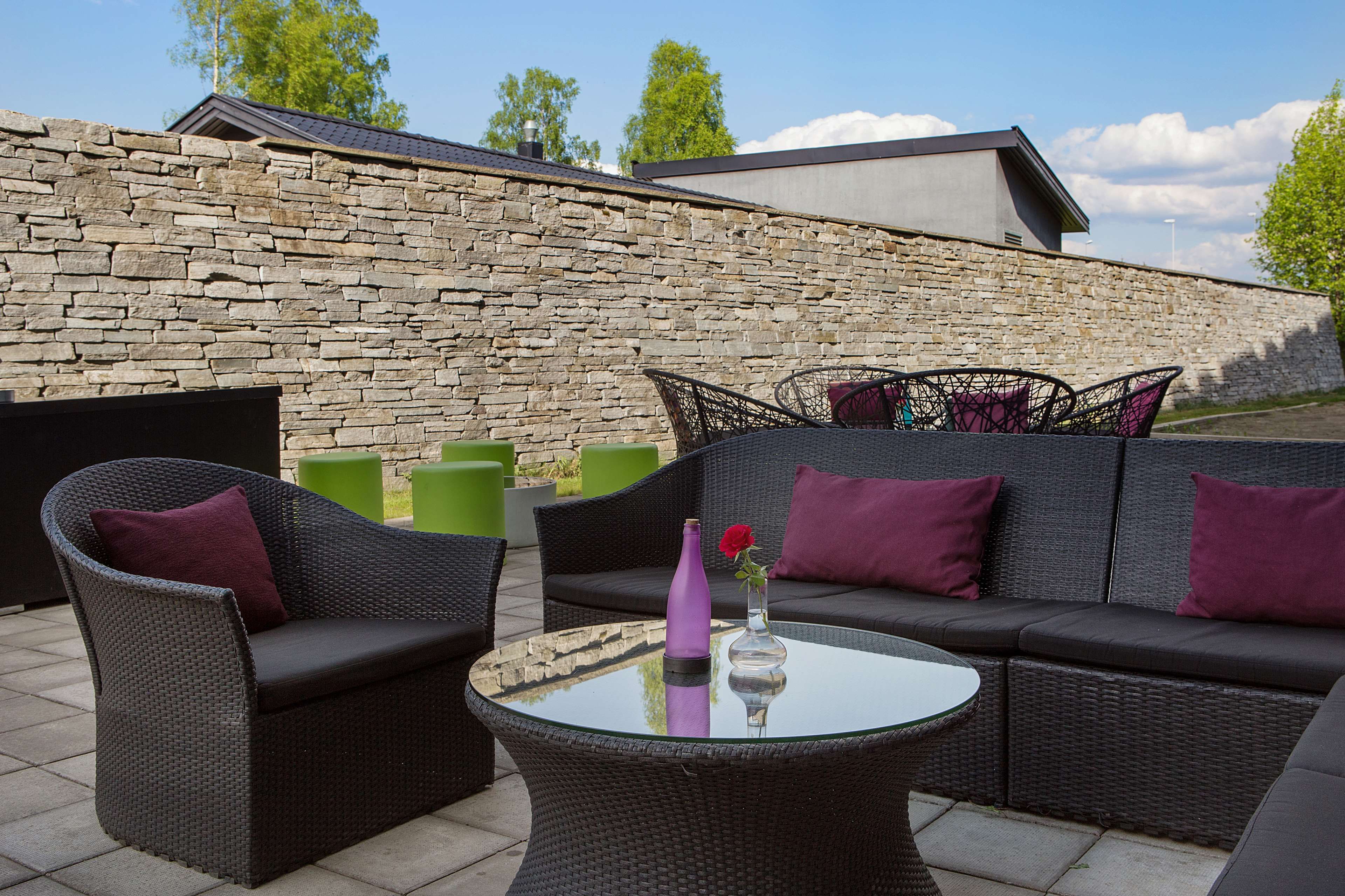 An outdoor patio area with wicker furniture, a glass table, and a stone wall in the background.