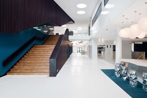 A modern interior with a wooden staircase, a reception desk, and a blue carpet. - Scandic Oslo Airport (Nannestad)