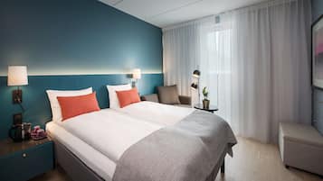 Una camera d'albergo con un letto grande, due comodini, un tavolino con una lampada e una sedia.