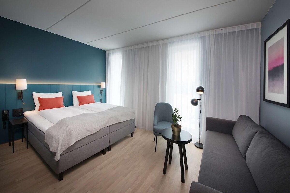 Una habitación de hotel con una cama, un sofá, una silla, una mesita y una lámpara.
