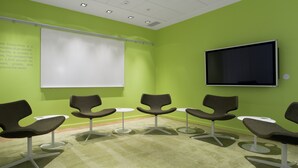 A conference room with green walls, a white projection screen, a flat-screen TV, and modern chairs arranged around a central table. - Scandic Oslo Airport (Nannestad)
