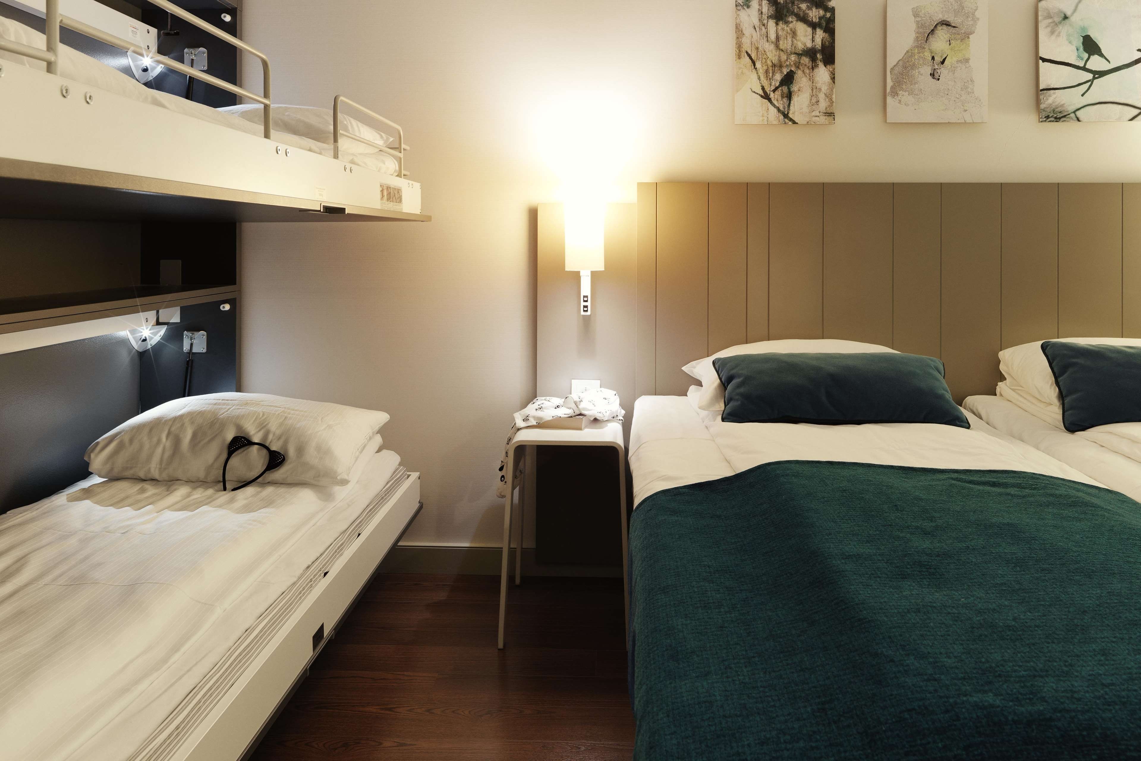 A hotel room with bunk beds, a bedside table with a lamp, and artwork on the wall.