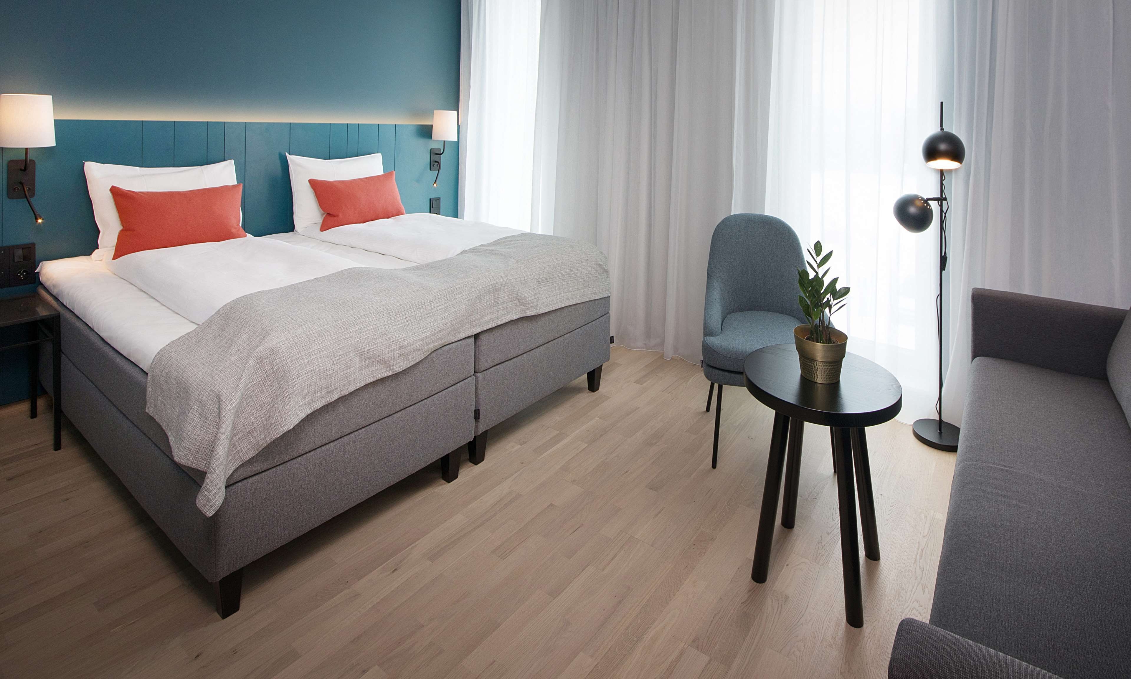 Ett modernt hotellrum med en säng, en stol, en soffa och ett litet bord med en växt.