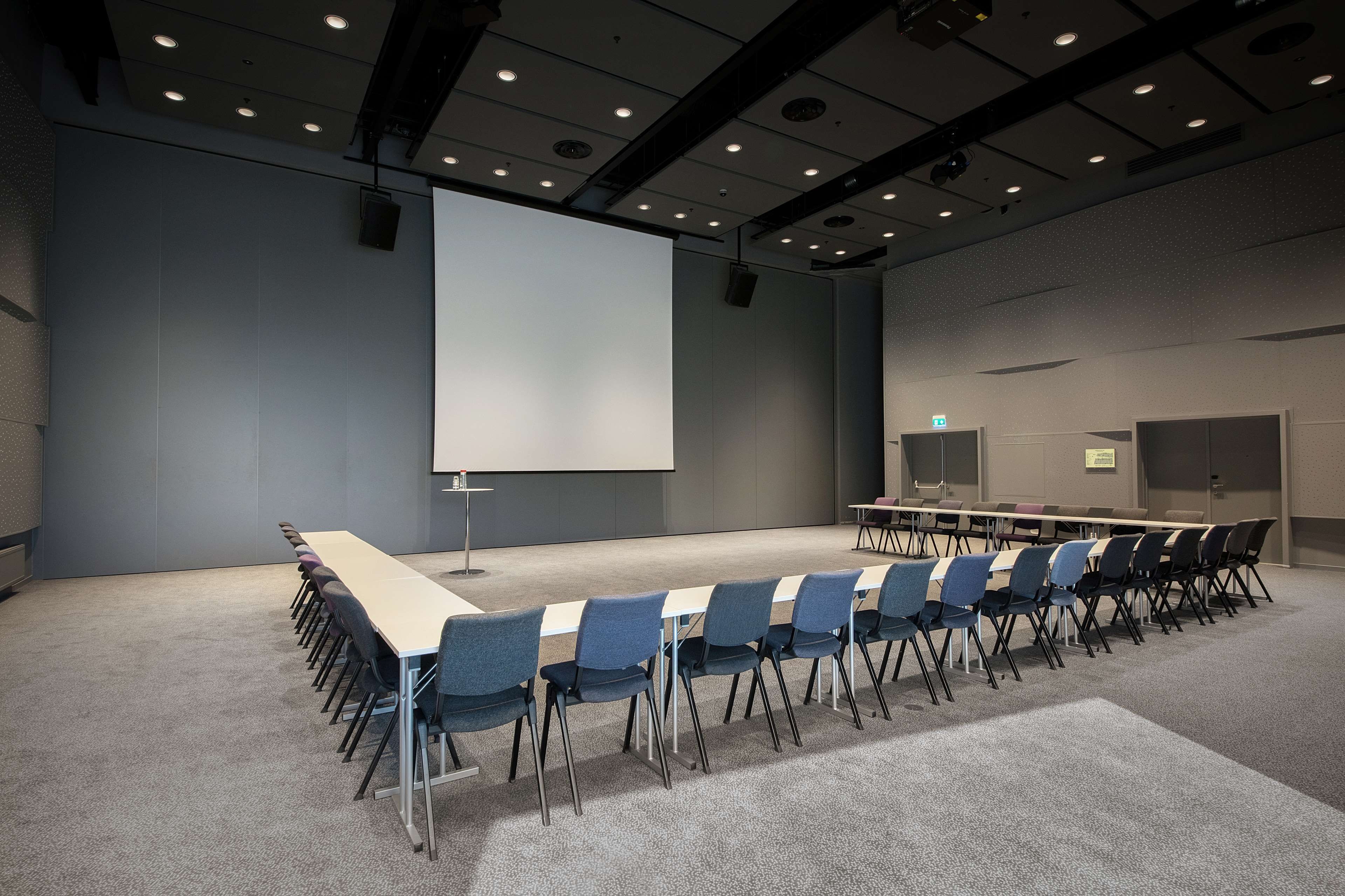 A conference room with a long table and chairs, a projector screen, and a carpeted floor.