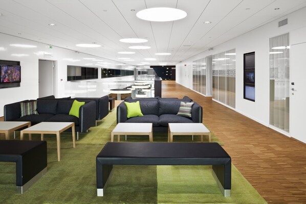 Ein moderner Arbeitsbereich mit einer langen Korridor, Besprechungstischen, Sofas und einem grünen Teppich.