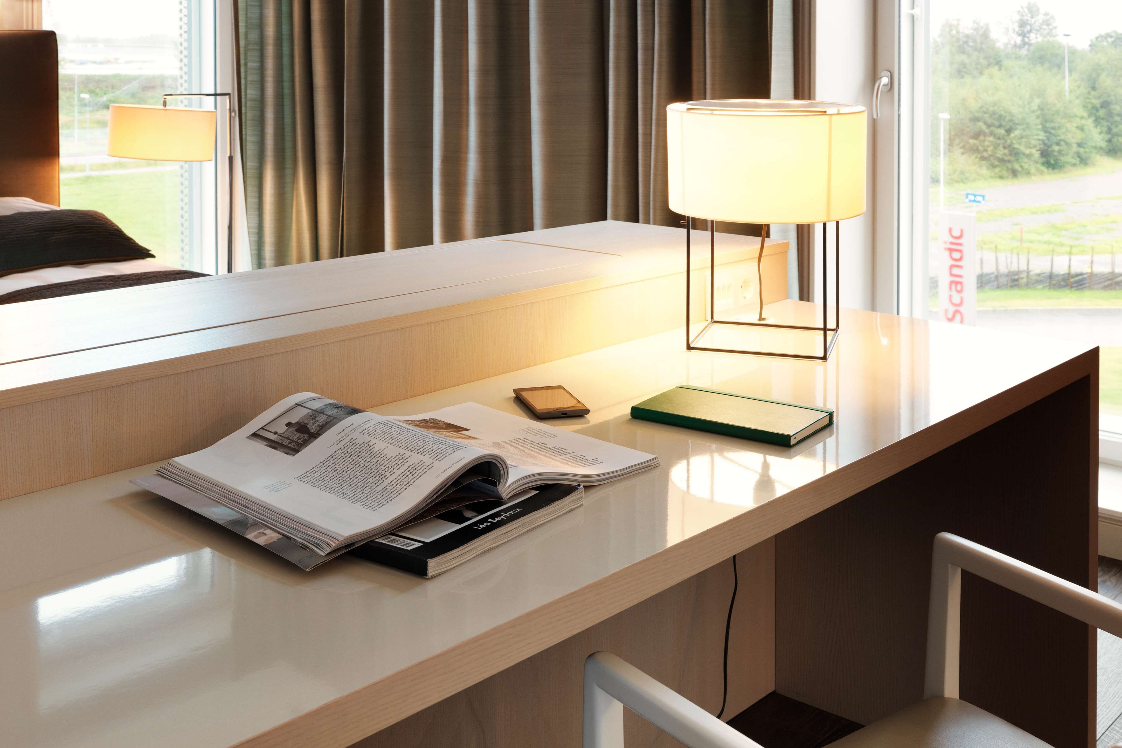 A hotel room with a wooden desk, a lamp, a book, and a smartphone.