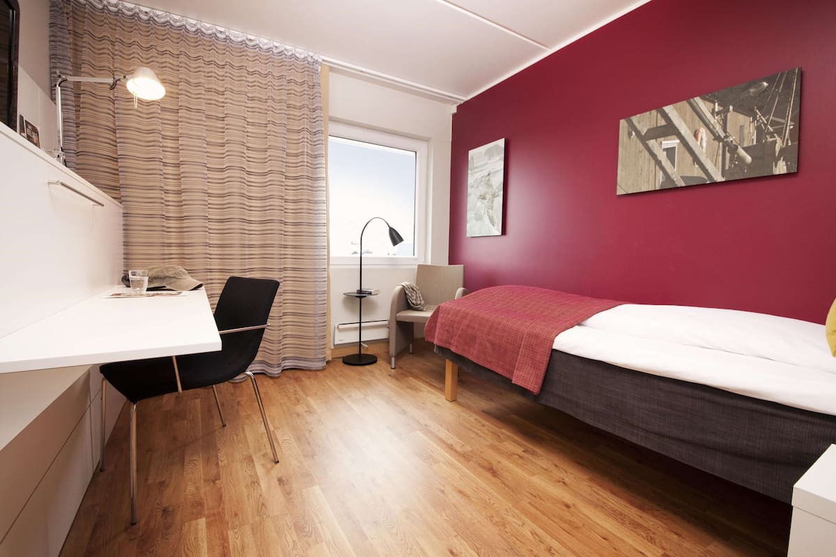 A modern bedroom with a bed, desk, chair, and a window with curtains.